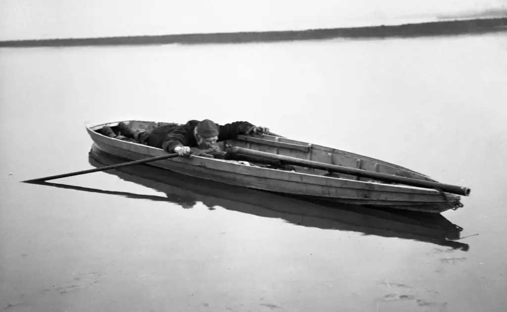 A man aiming a punt gun mounted on a punt boat