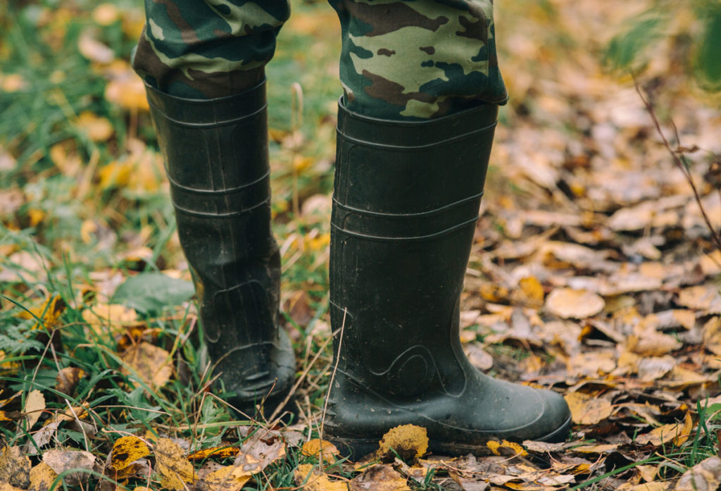 Male hunter stands in rubber hunting boots while in the woods