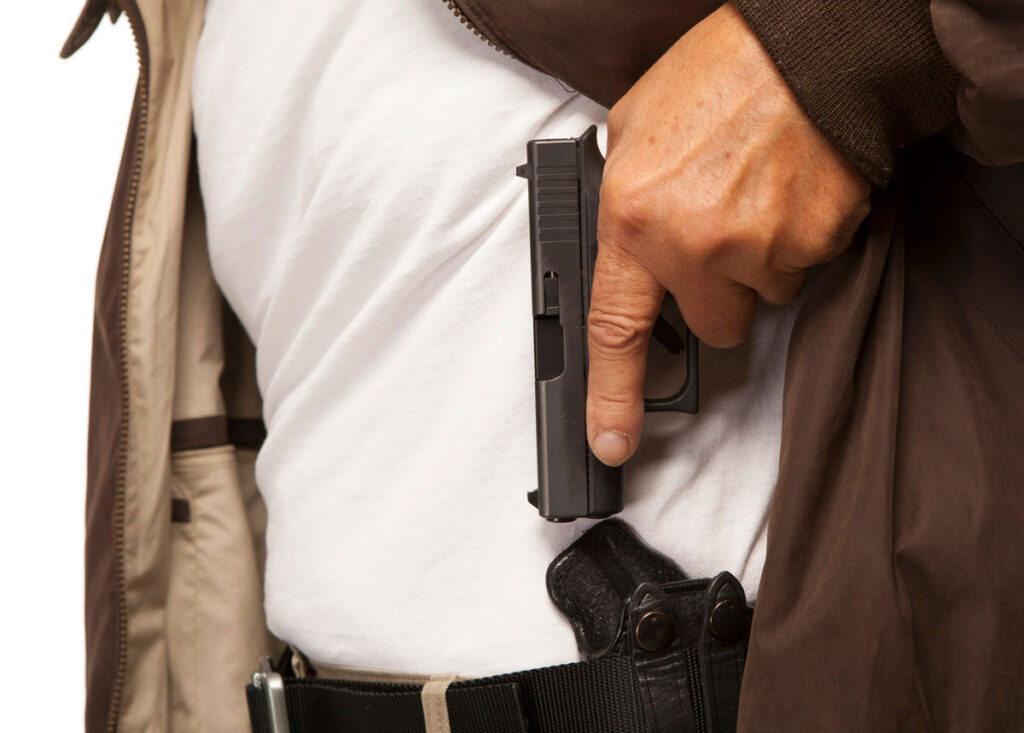 man pulling a pistol from a concealed carry holster in his jacket